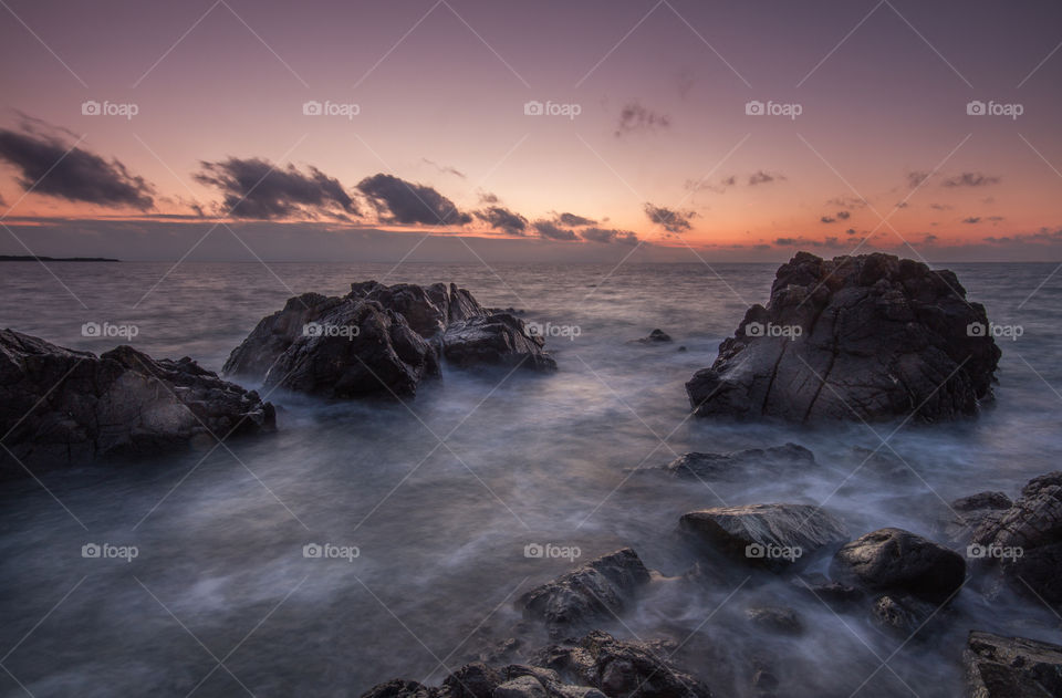 A rugged coastal scene at sunrise with water flowing over harsh rocks.