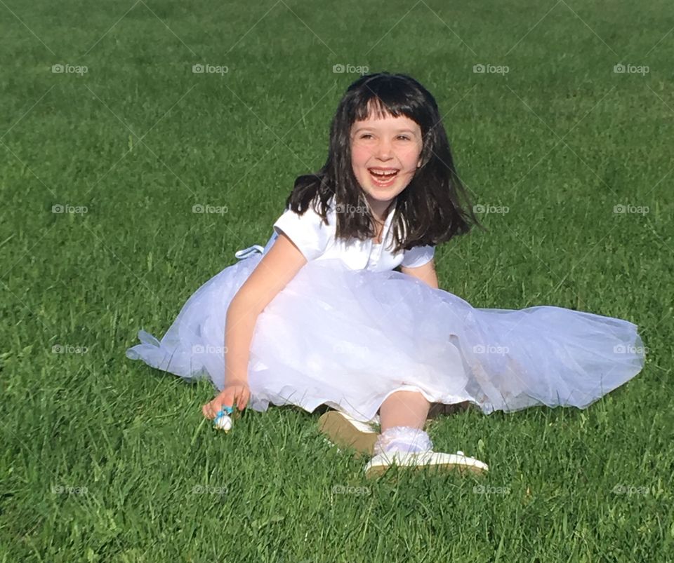 Little girl in a white dress laughing in a field of grass