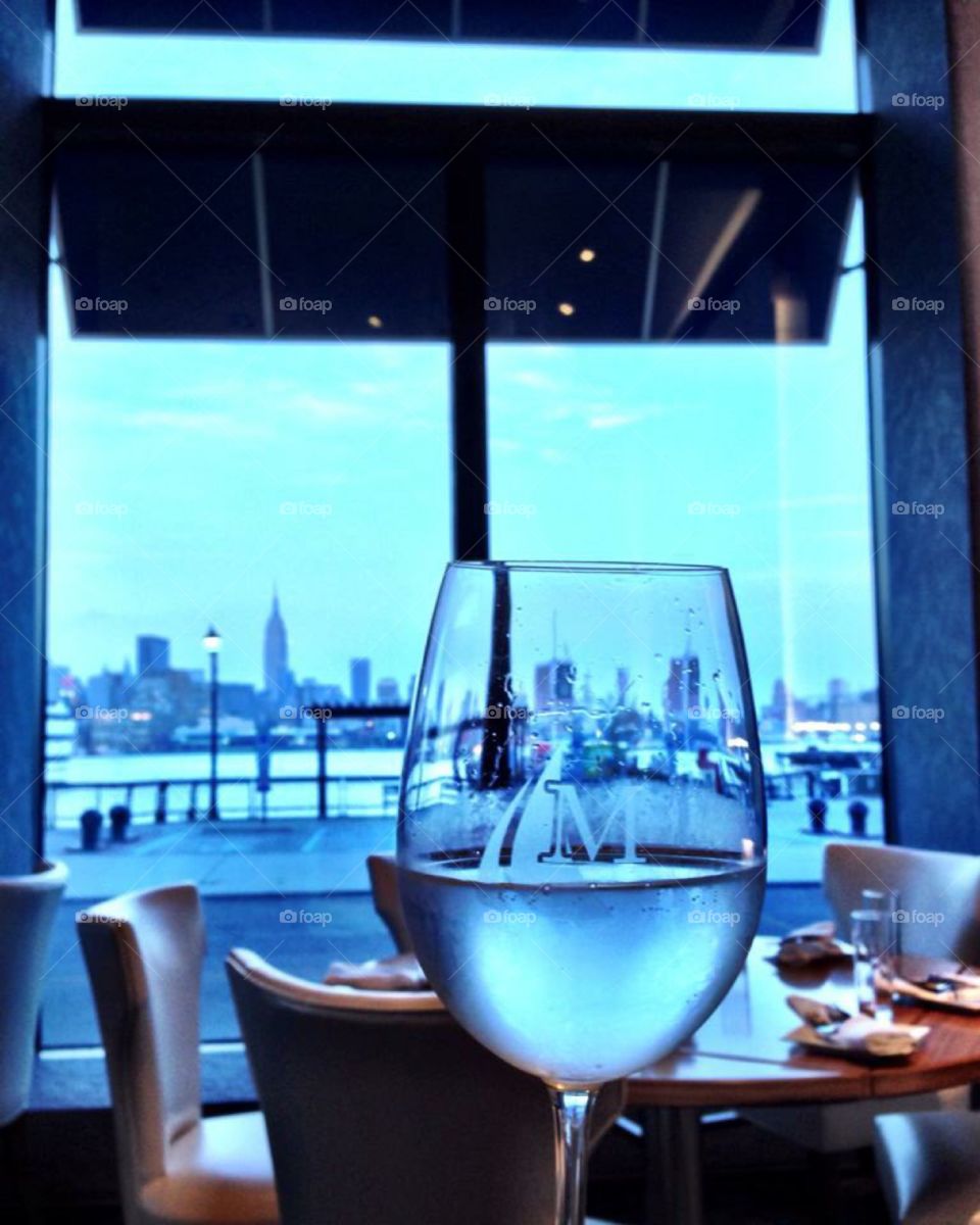Toast to New York City . Raised glass with New York City skyline on the background. Hudson River view and Empire State Building.
