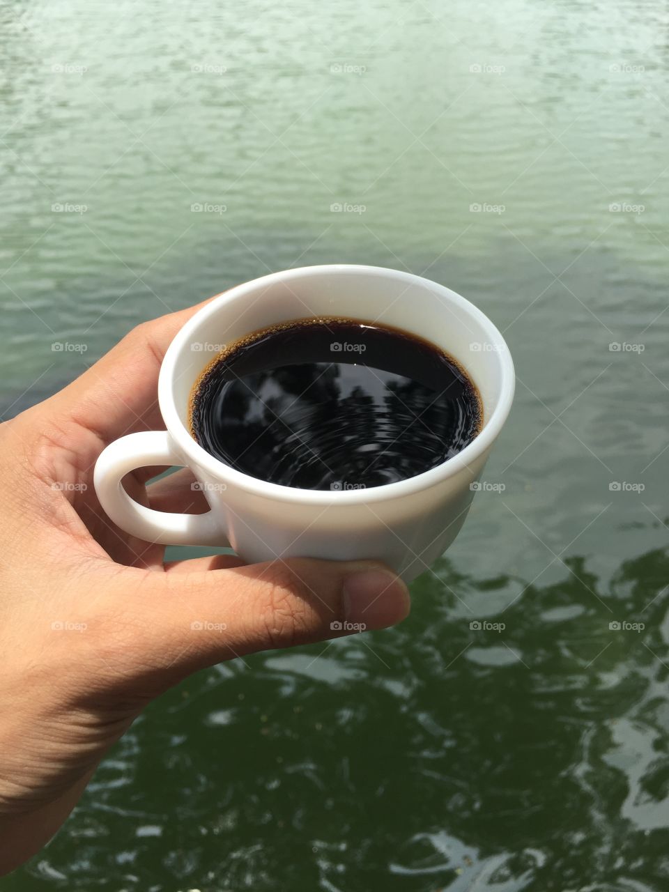 A cup of black coffee in hand, water background 