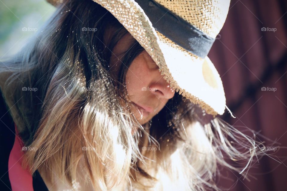 Woman with brown hair wearing a straw hat in the sunshine 