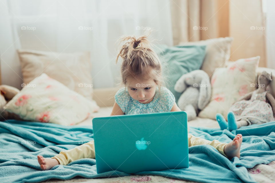 Little sisters with gadgets(laptop and tablet) in the bed.