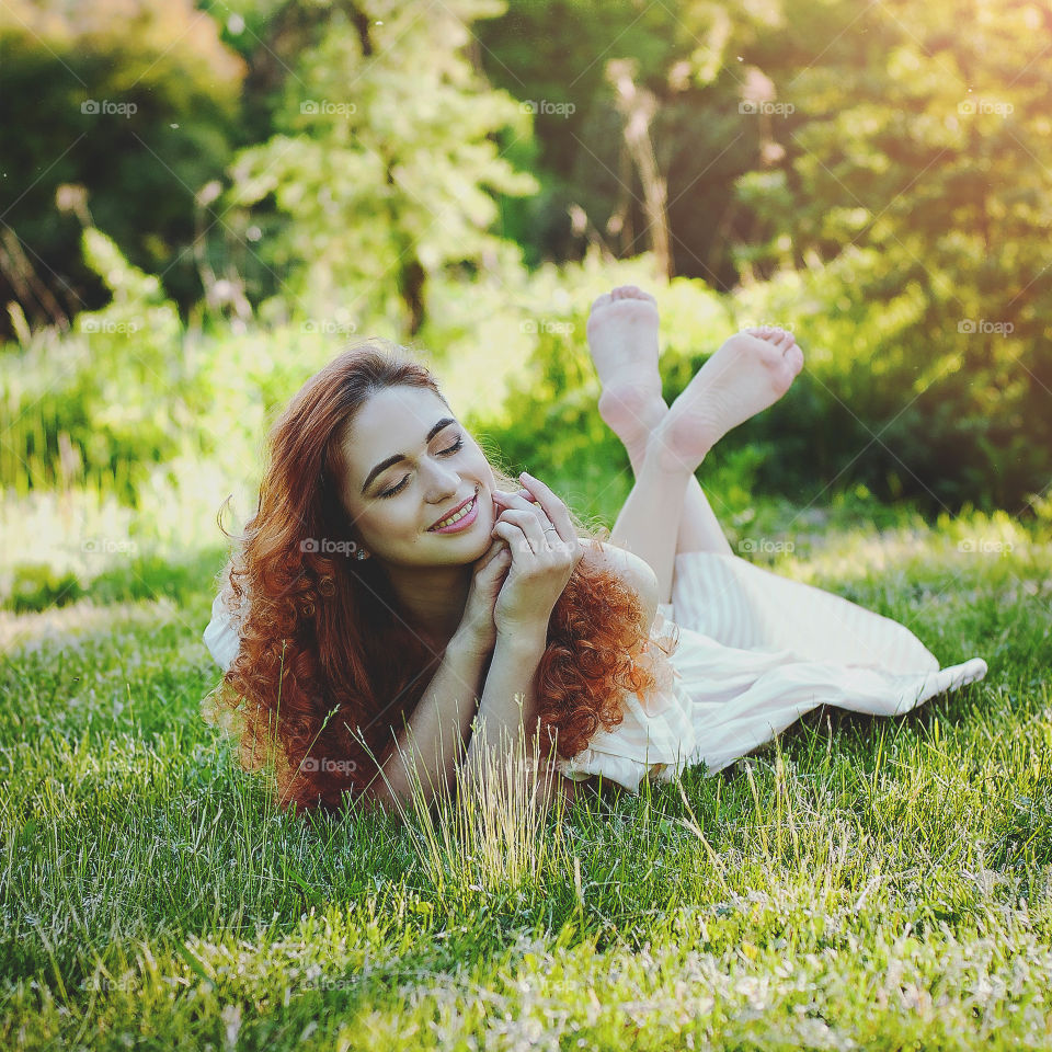 Young attractive redhead woman relaxing and sitting in the green grass in the nature at spring.