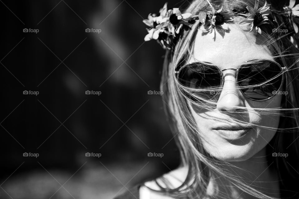 Black and white closeup retro vibe portrait of a young woman wearing a flower crown and sunglasses on a sunny summer day 