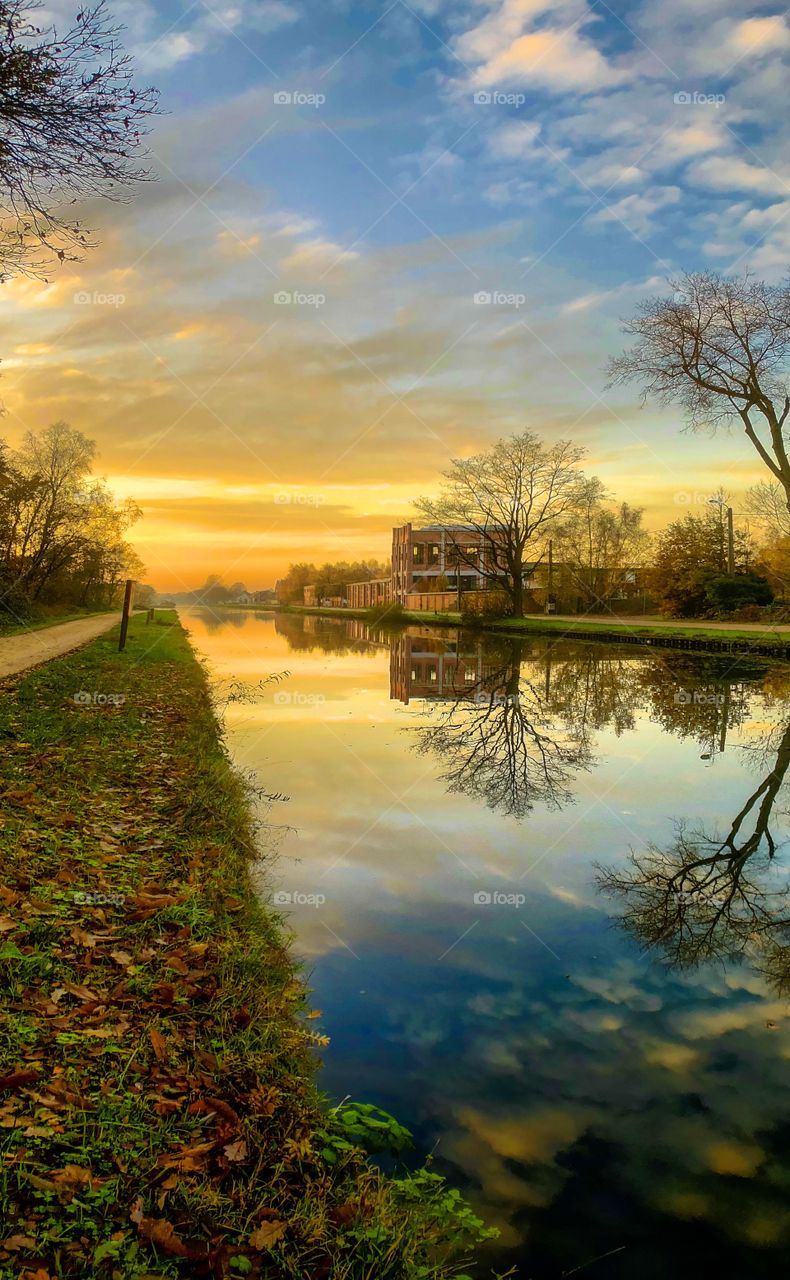 Dramatic and colorful sunrise or sunset over a Countryside river or canal landscape with the sky and clouds reflected in the water