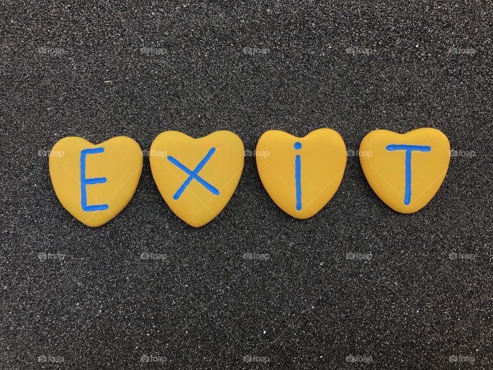 Exit word with yellow colored heart stones  over black volcanic sand 