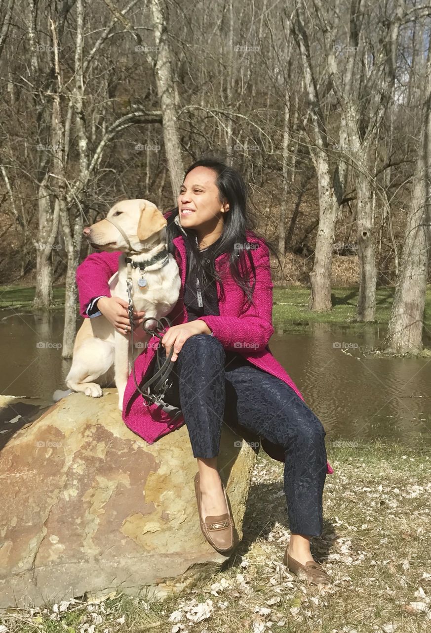 A spring walk with your dog, yellow Labrador retriever sitting on a rock with a young lady 