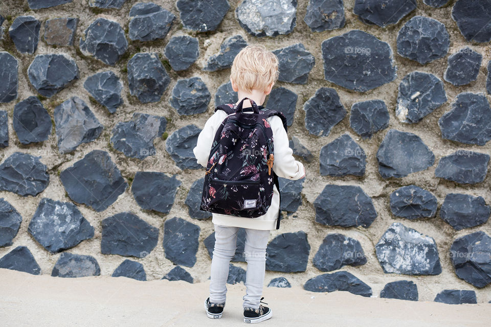 A boy with bis backpack standing in front of a wall
