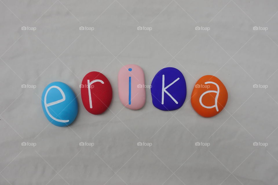 Erika, feminine given name on colored stones over white sand