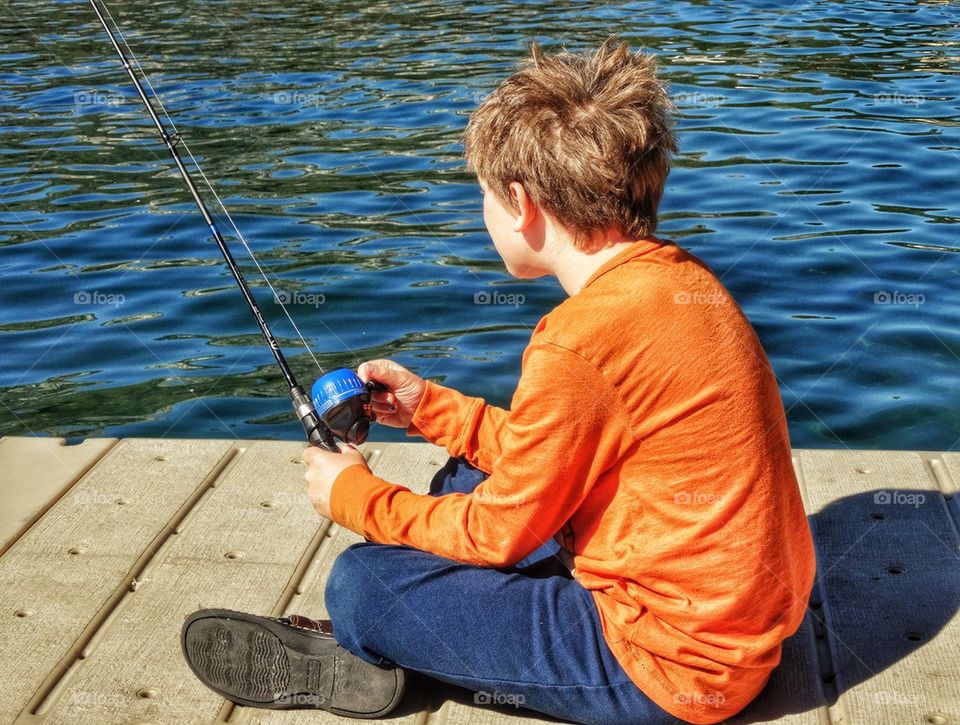 Young Boy Fishing From A Pier. Boy Patiently Waiting For Fish To Bite