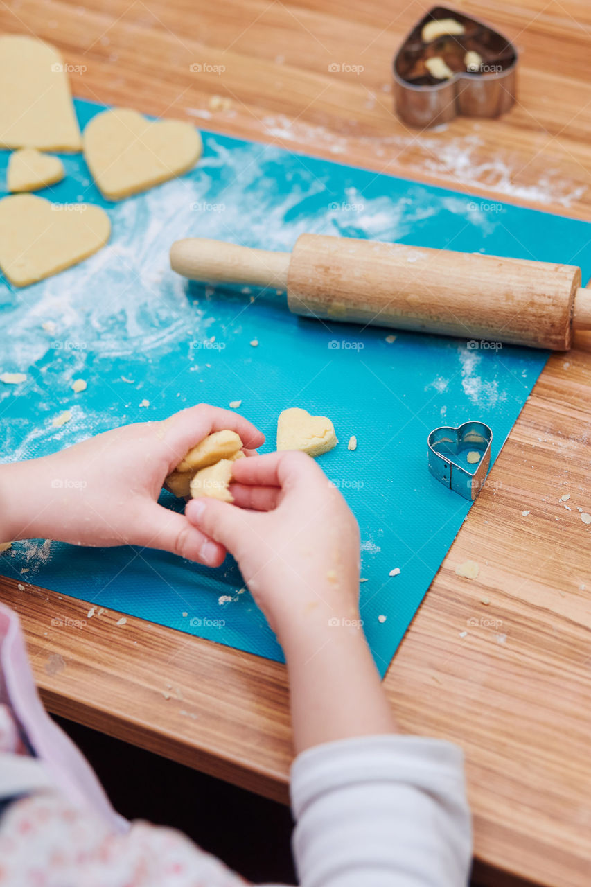 Little girl cutting the dough to heart shapes for the cookies. Kid taking part in baking workshop. Baking classes for children, aspiring little chefs. Girls learning to cook