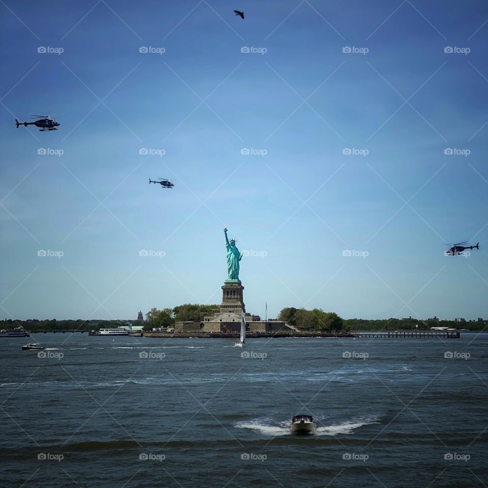 Statue of Liberty in New York harbor surrounded by boats, helicopters and a bird