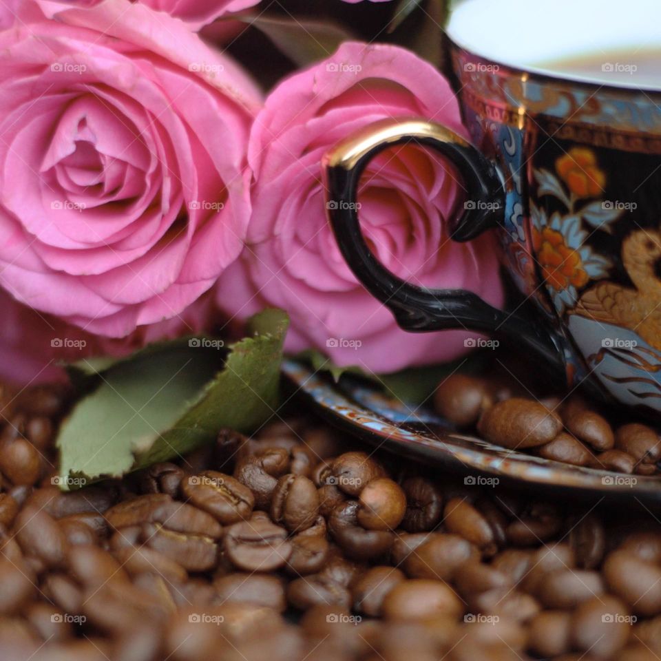 morning coffee in the beautiful cup surounded with coffee beans and pink roses.