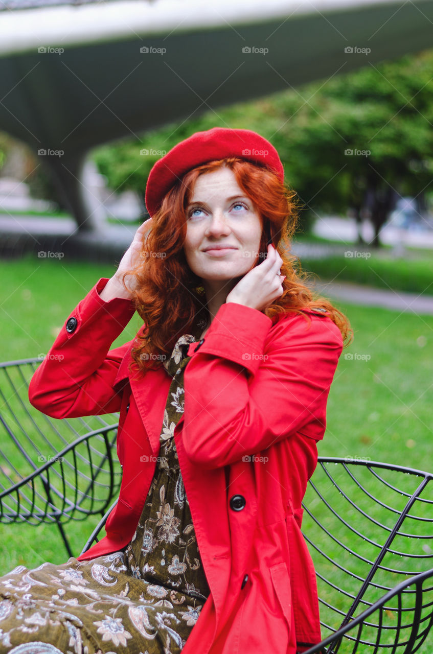 Portrait of a young redhead curly woman in red coat with freckles and blue eyes walking in autumn park. Happy people.