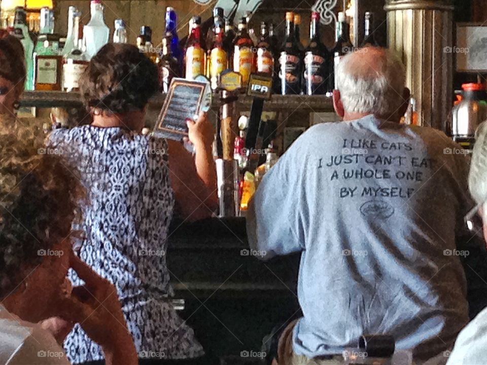 I like cats....bar scene. Couple at bar, back of man's tee shirt reads, ' I like cats, I just can't eat a whole one'