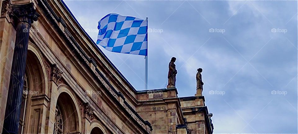 High up on the rooftop of the “Maximilianeum” in “Munich”, a large palatial building that houses the “Bavarian State Parliament”, the “Landtag” the white and blue Bavarian flag waves vivaciously in the wind. 2024. Hypnotic Productions