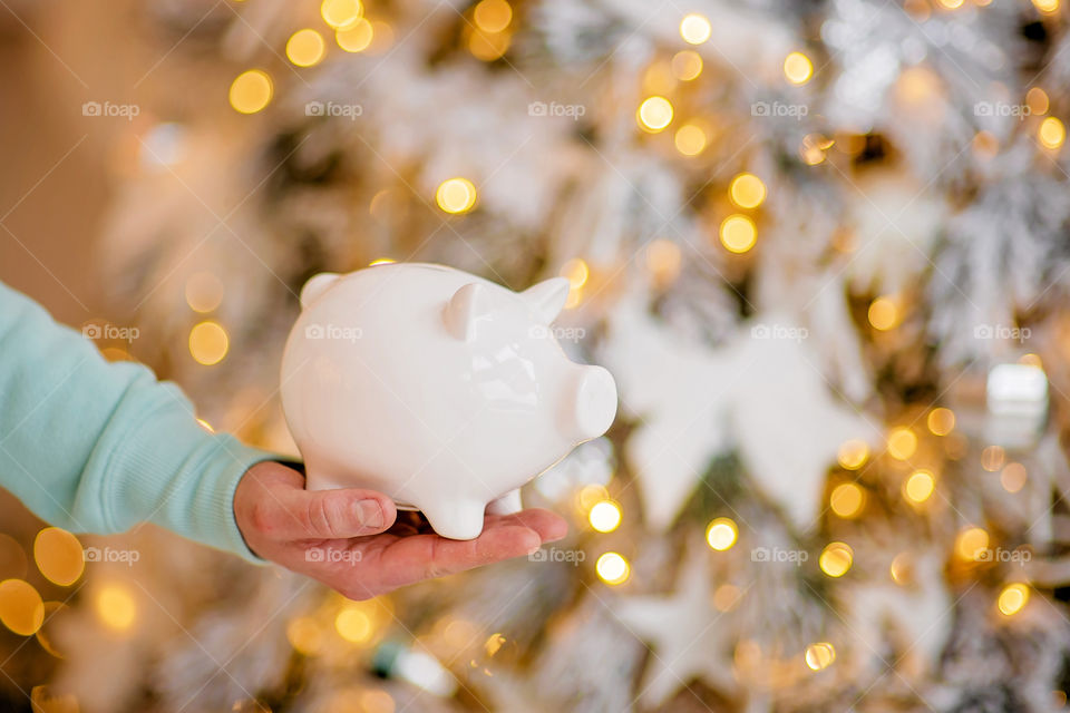 piggy bank with 100 dollars banknote in festive New Year atmosphere of scenery.  Magical bokeh with Christmas tree and bright lights.