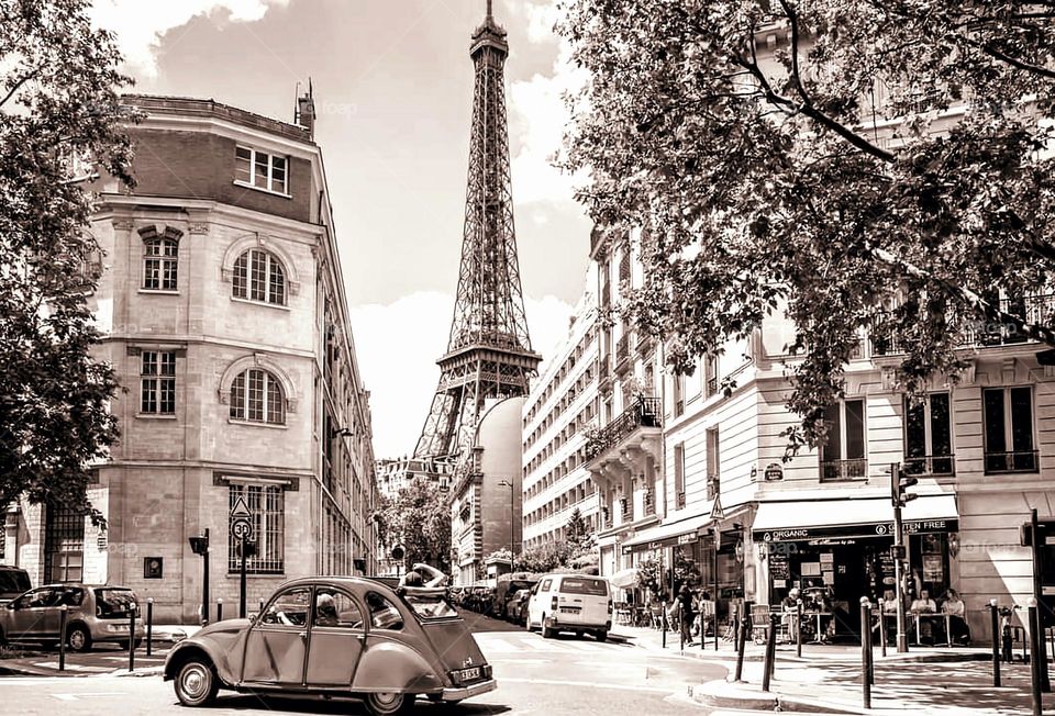 Vintage sepia shot of a Citroen 2CV passing on a main road of Paris with a view on the Eiffel Tower across a perpendicular street