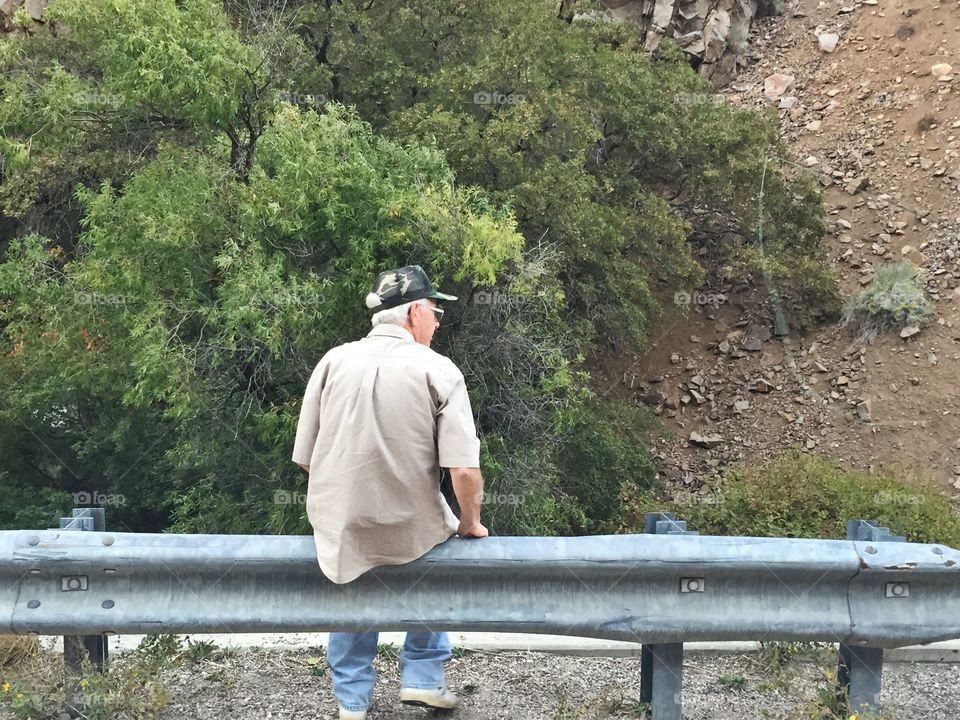 An elderly gentleman sits alone on the side of the road. 