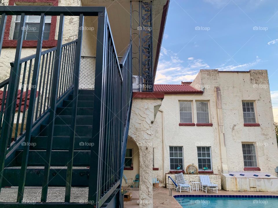 White and red spanish old style architecture residential large house built in the early 1900s. Many windows on the side of the house low angle with aging signs with charming pretty style and beautiful landscaping with pool and chairs with a staircase