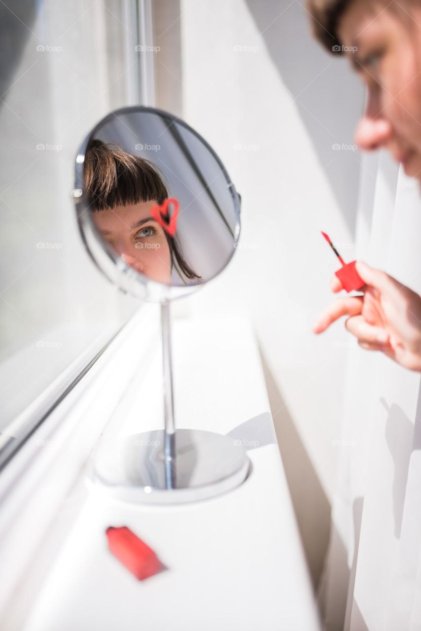 Girl looks at herself in the mirror while drawing a lipstick heart as a reminder to love herself
