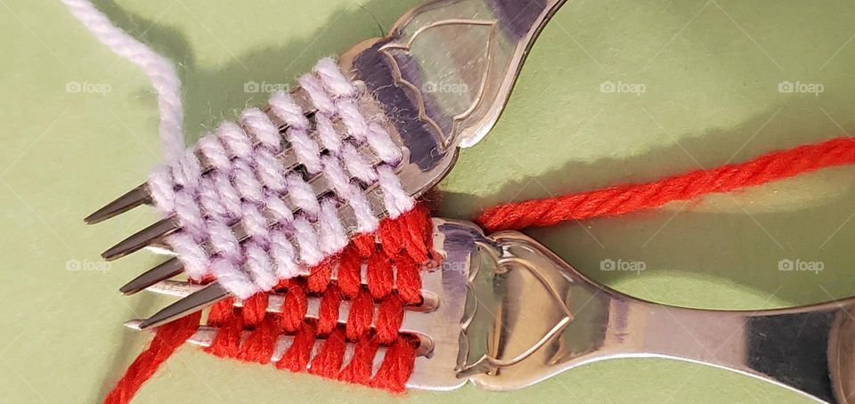 two silver forks weaved with yarn, lavender & red, laying overlapping the other