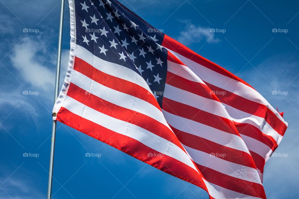 Horizontal photo of a red, white and blue American flag waving in the breeze against a blue sky with white clouds