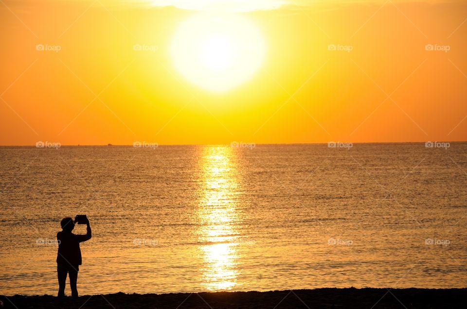 A silhouetted adult female uses a tablet to photograph the sunrise at Hollywood Beach Florida
