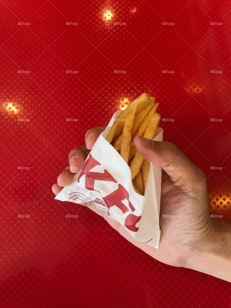 consumer holds KFC french fries with red table on background