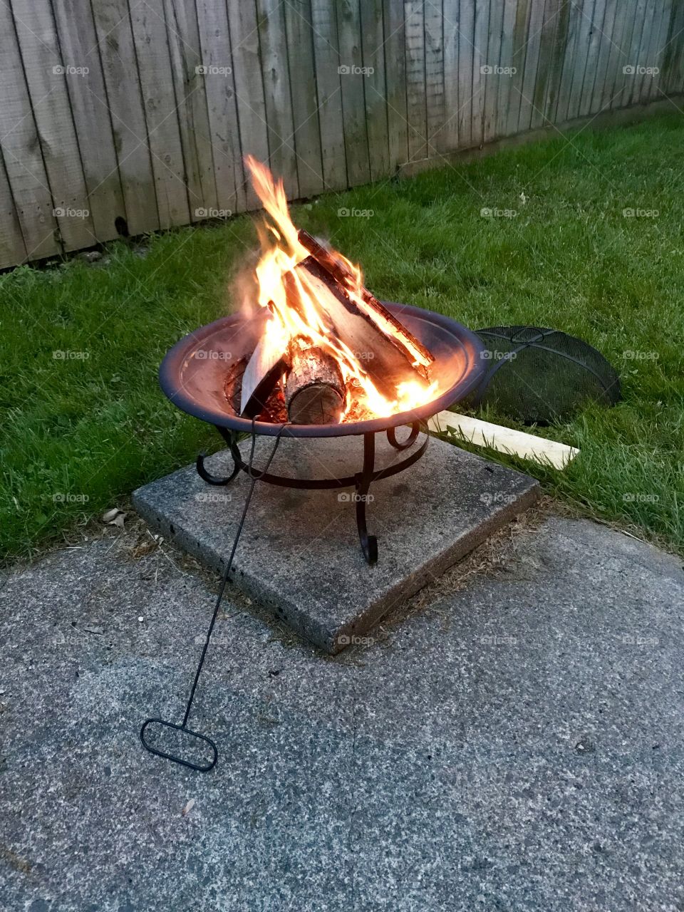 Fire pit in the back yard w flames and poking stick