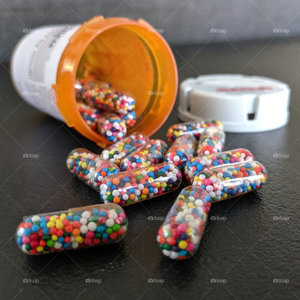 Sprinkle-filled sugar capsules spilling out of prescription container.