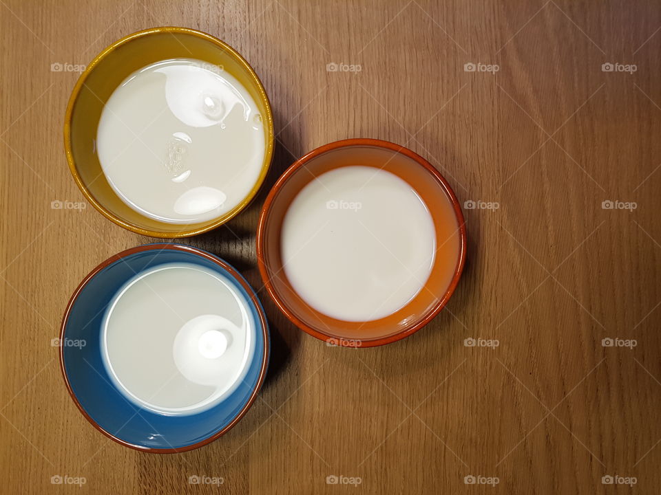 Overhead shot of three colors bowls with milk flat lay on a wooden table, view from above