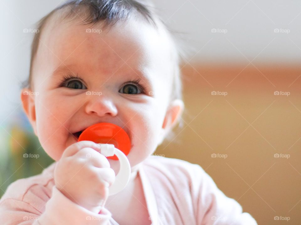 Portrait of one beautiful and cute caucasian baby girl with a happy smile on her face, looking to the side and holding a pacifier in her mouth, standing in a napkin in the early morning, close-up side view. Happy kids concept.