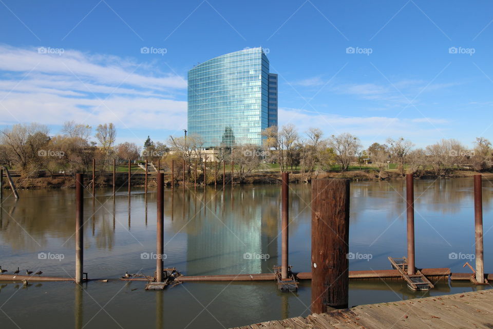 standing on the Riverwalk in Sacramento California looking across the river at a glass high-rise building with blue skies in the background.