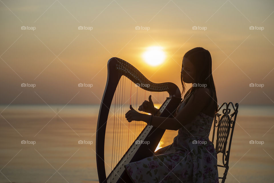 Young woman playing celtic harp at the sea during sunset