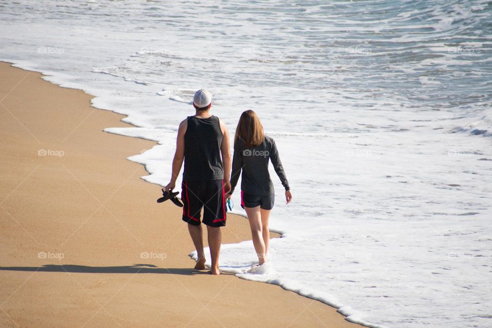 A couple walking along the beach with water at their feet