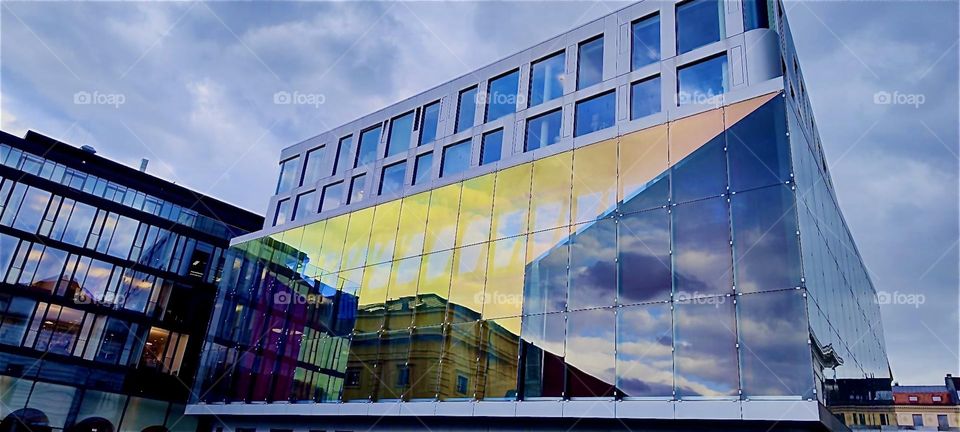 An ultramodern building in the inner city of “Munich”, capitol of “Bavaria” gets our attention by reflecting what is in the heavens, clouds and surrounding houses. 2024. Hypnotic Productions