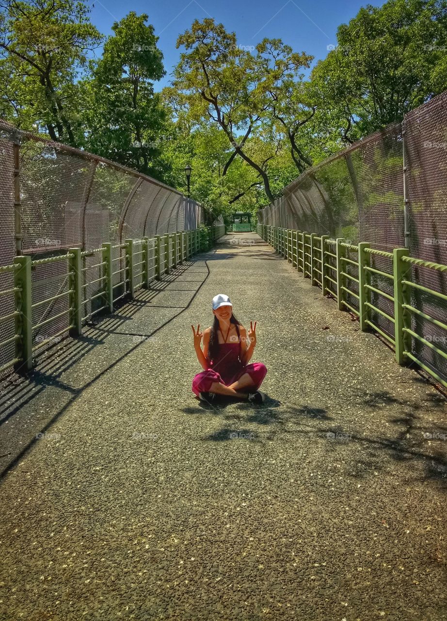 The woman wearing a white hat sitting at the center of the bridge with two sign of peace. 