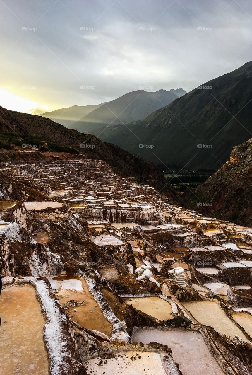 The sun light illuminates bright brown and red colors over salt mines in the mountains of Cuzco, Peru. 