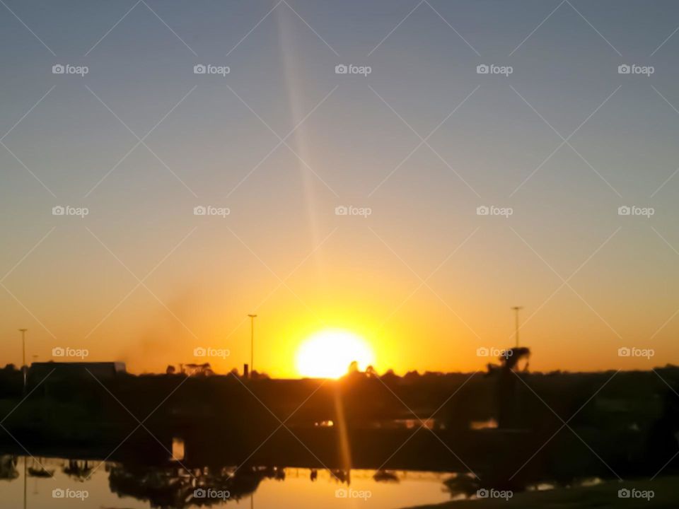 Sunset in the city provides a sunset with sunbeams, reflection of trees in the river and the sky in orange tone.
Por do sol na cidade proporciona um entardecer com raios solares, reflexo das árvores no Rio e o Céu em tom alaranjado.