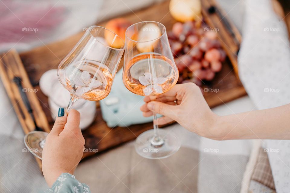 Two women hands hold glasses with wine. Picnic in public park