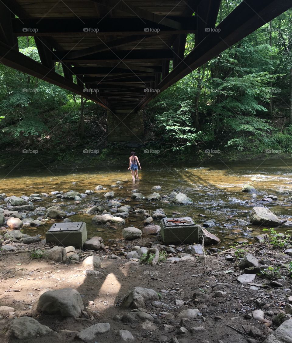 Woman under a bridge standing in a creek