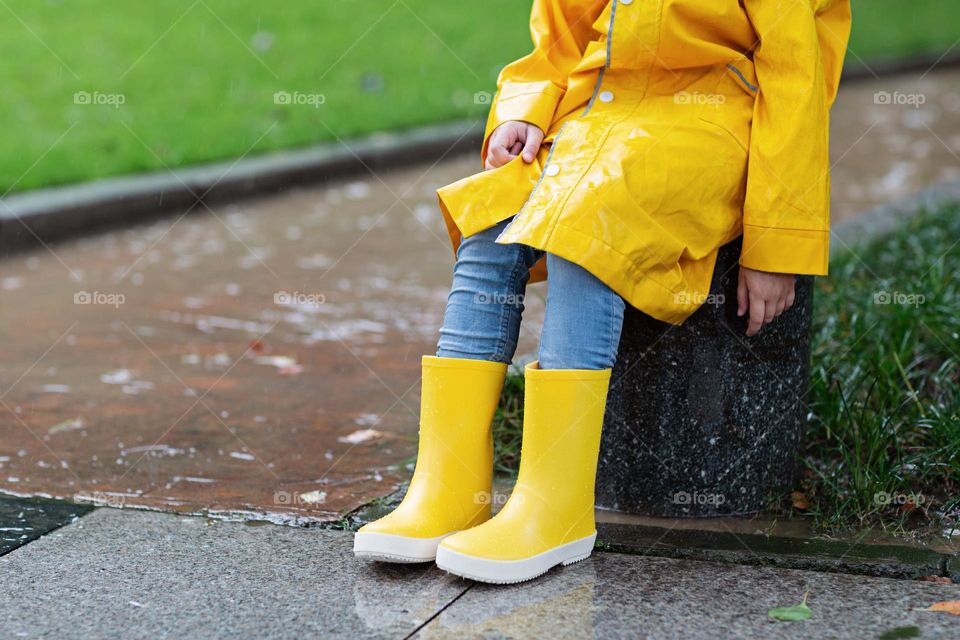 Kid wearing yellow raincoat and rubber boots outside 