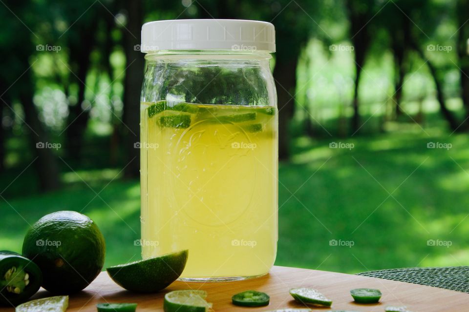 Refeshing lime-and-jalepeño-flavored kombucha, rebottled in a quart-size mason jar for a second ferment, with slices of lime and jalepeño on a bamboo cutting board, against a blurred outdoor background in summer