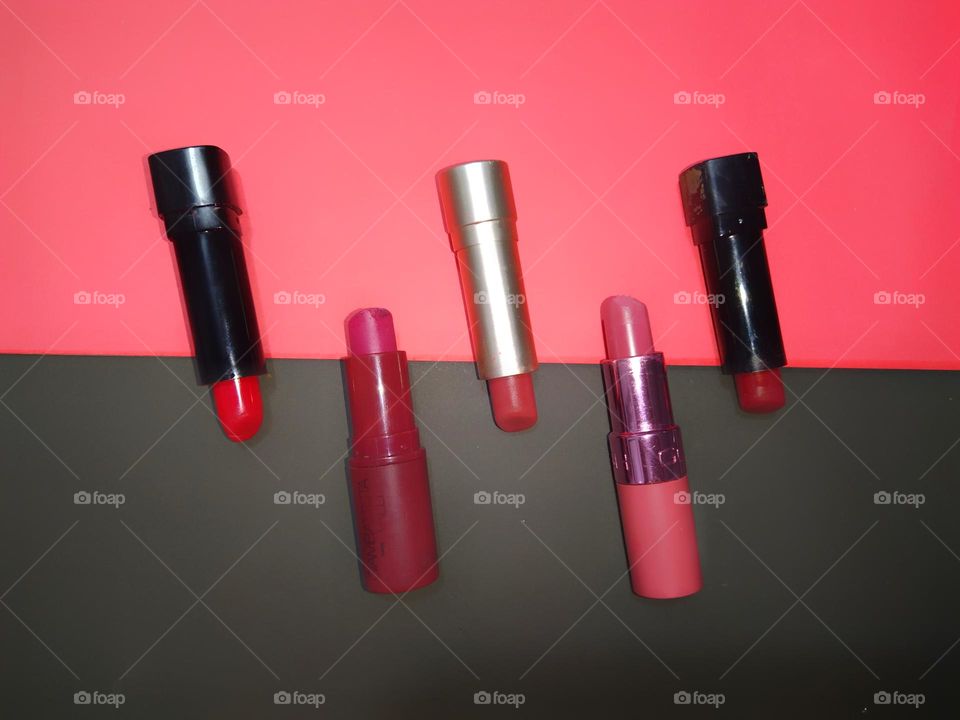 Close view of lipsticks arranged parallelly against a pink and black background captured from above.