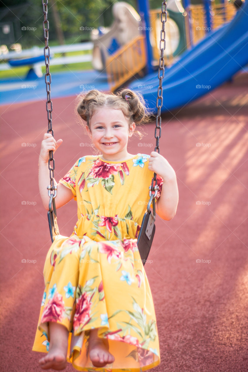 Young Girl Swinging at the Playground in Yellow Floral Dress