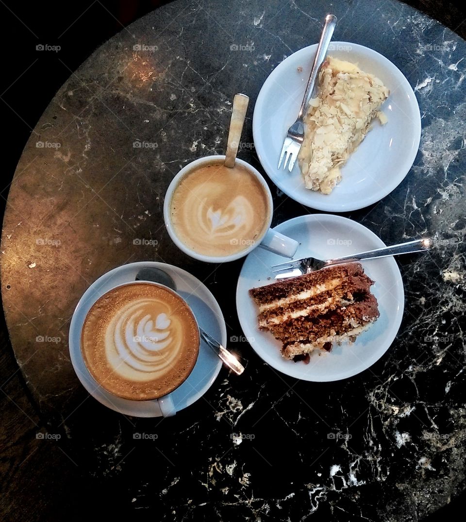 Two slices of delicious cake on white plates with two cups of coffee latte