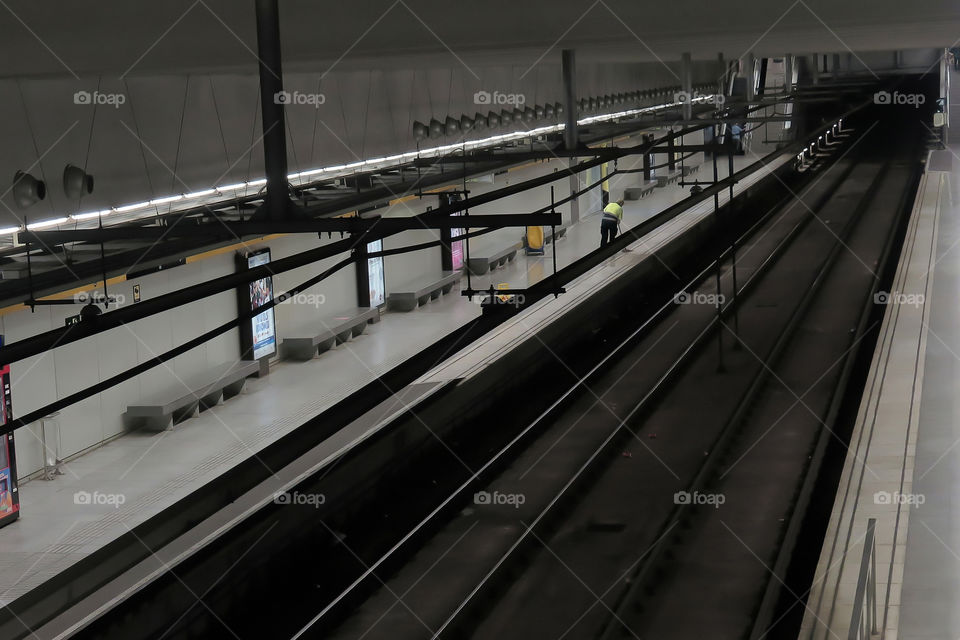 A worker is sweeping the empty platform of a Barcelona metro station in Spain at night.