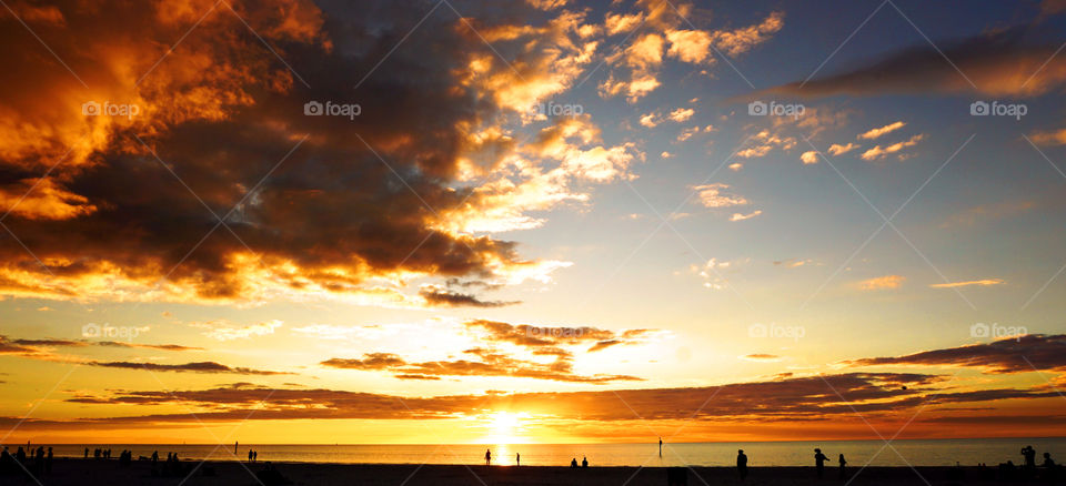 Golden and blue sundown with moving silhouettes on the beach
