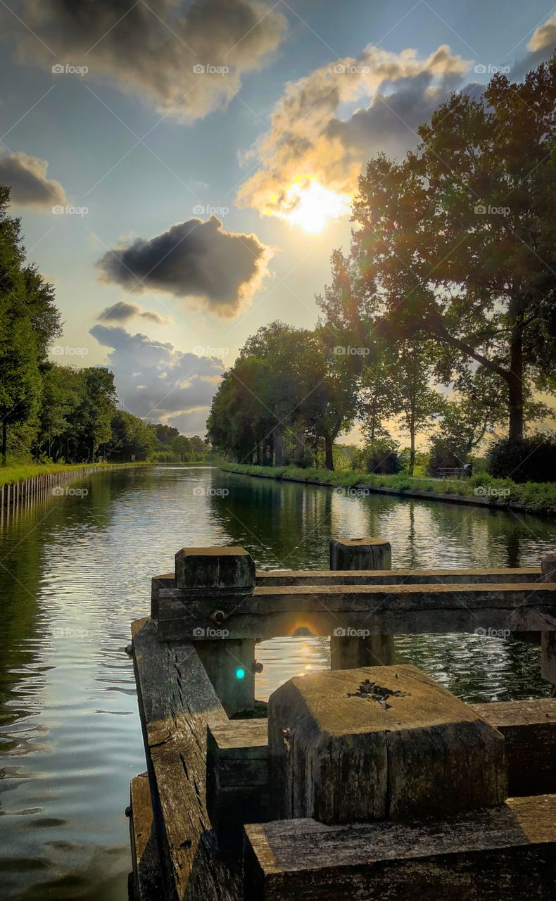 Dramatic sunset or sunrise over a tree lined river landscape as seen from a wooden bridge with the trees and the sky reflected in the water